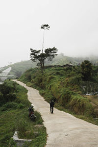 People on footpath by road against sky