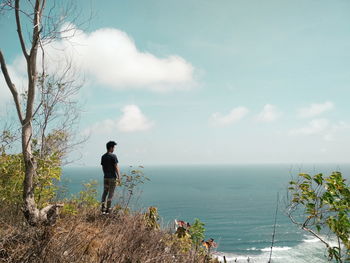 Rear view of man standing by sea against sky