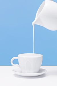 Close-up of jug pouring milk into coffee cup on table