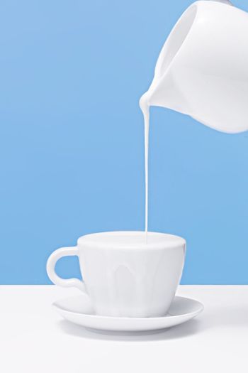 Close-up of jug pouring milk into coffee cup on table