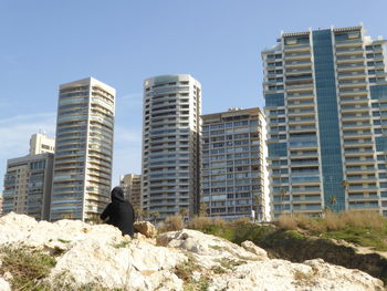 Rear view of man sitting against modern buildings
