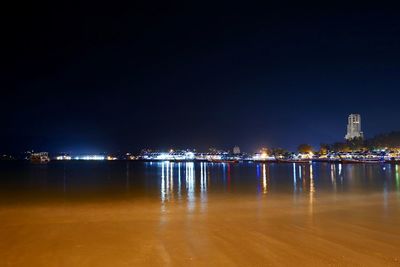 Illuminated buildings by sea against clear sky at night