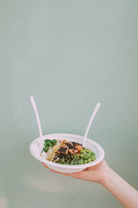 Cropped hand holding salad in bowl against wall