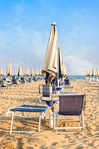 Deck chairs on beach against sky