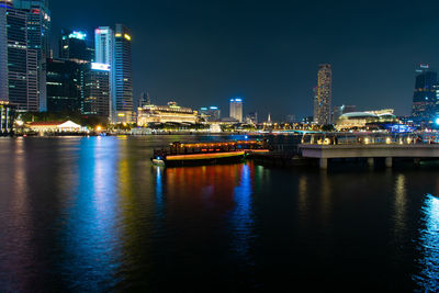 Illuminated buildings by river against sky at night