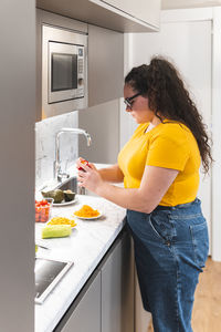 Young woman grating cheese standing in kitchen at home