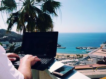 Cropped image of person using laptop by smart phone on sunny day