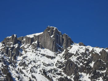 Low angle view of snowcapped mountains against clear blue sky