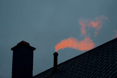 Low angle view of smoke emitting from chimney against sky at sunset