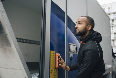 Confident male worker pushing button on delivery van in city