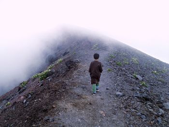 Rear view of man walking on mountain against sky