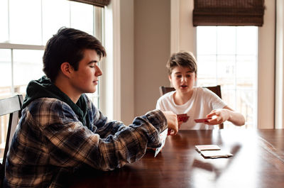 Two teenage boys playing cards at the kitchen table together.