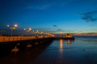 Illuminated pier over sea against sky at sunset