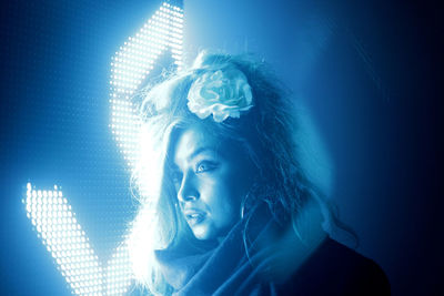 Close-up of young woman wearing flower by blue illuminated light