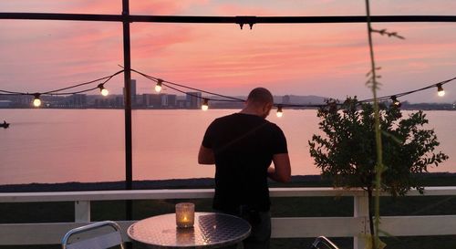 Man standing by railing at balcony against sky during sunset