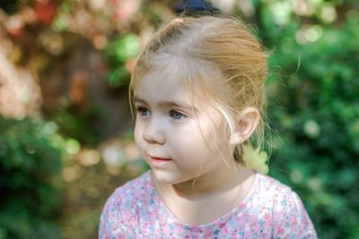 Adorable little girl with blonde hair looking away in beautiful garden setting