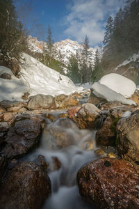Stream flowing through rocks against sky during winter