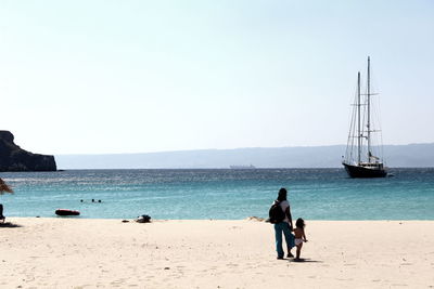 Rear view of mother and child at beach against clear sky