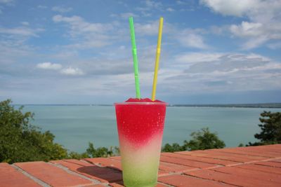 Close-up of drink on table by sea against sky