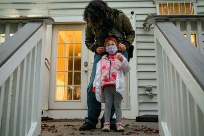 Father securing face mask on daughter before trick or treating covid