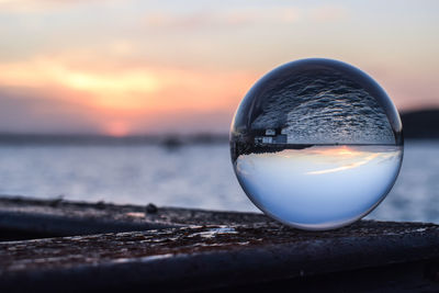 Close-up of crystal ball in sea against sunset sky