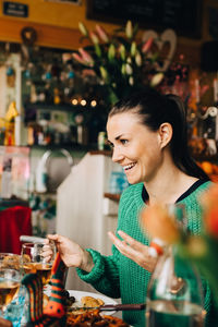 Smiling young woman sitting at table in restaurant during dinner party