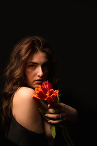 Close-up of woman holding red rose against black background