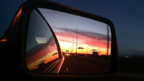 Close-up of side-view mirror against sky at sunset