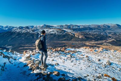 Rear view of man standing on snowcapped mountain against blue sky