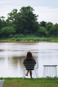 Rear view of a woman sitting alone in the yard by the river