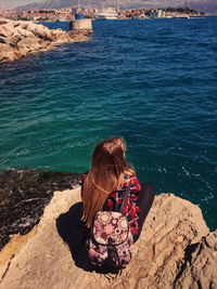 Rear view of woman sitting on rock by sea