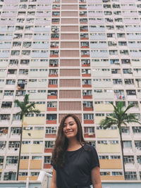 Portrait of smiling young woman standing against buildings