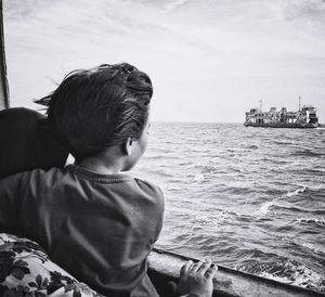 Rear view of boy in boat looking at sea