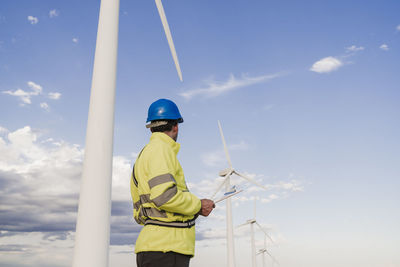 Engineer wearing reflective clothing looking at wind turbines by sky