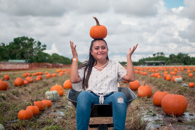 Portrait of smiling young woman standing by pumpkins on field against sky