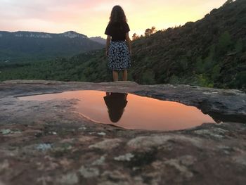 Rear view of woman standing by mountain against sky during sunset