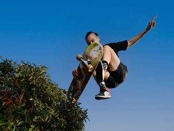 Low angle view of boy jumping against clear blue sky