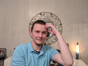 Portrait of young man sitting against wall at home