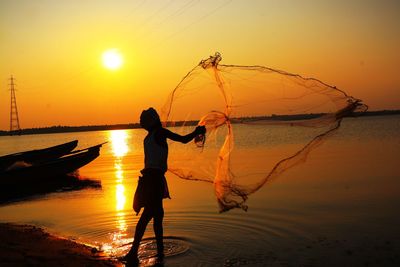 Silhouette man with arms outstretched standing at sunset