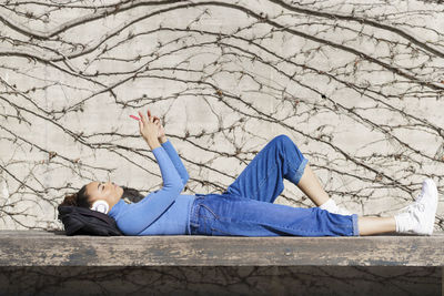 Woman with backpack and headphones using mobile phone while resting on bench