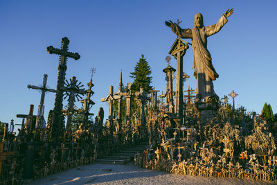 Statue and cross at cemetery against clear sky