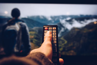 Cropped image of hand holding remote control in front of television set