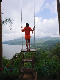 Rear view of woman standing on swing against forest