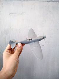 Close-up of hand holding airplane against wall