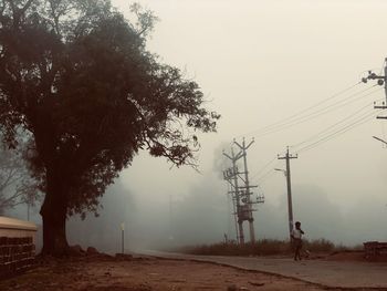 Electricity pylon on land against sky during foggy weather