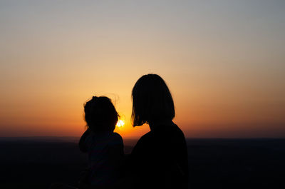 Silhouette women on shore against sky during sunset