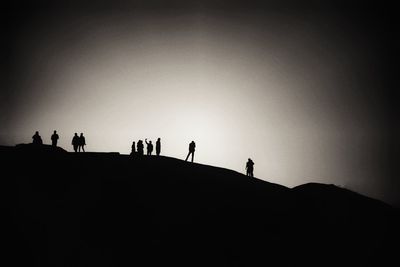 Low angle view of silhouette people walking on mountain against clear sky during sunset