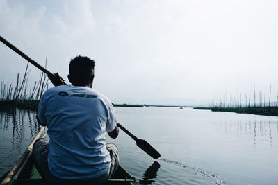 Rear view of man fishing in lake against sky