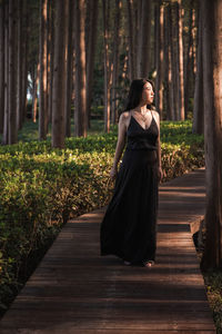 Full length of woman on wooden path in forest looking into sunlight