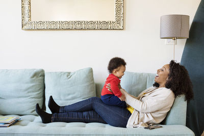 Happy woman playing with son while sitting on sofa at home